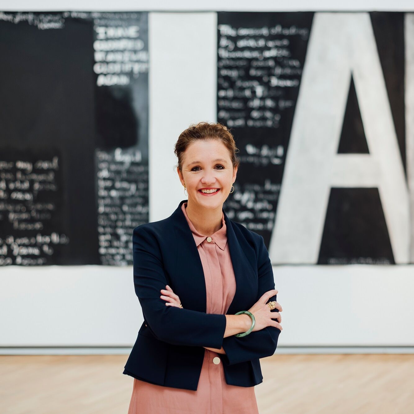 Image: New Auckland Art Gallery Director Kirsten Paisley
Image Credit:  Photography by Rohan Thomson. Artwork shown in background: Colin McCahon, Victory over death 2, 1970, National Gallery of Australia. Gift of the New Zealand Government 1978